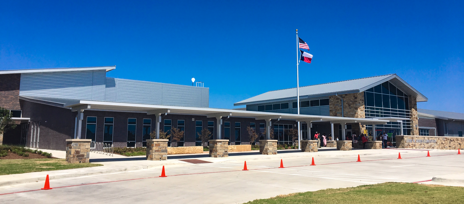Exterior of Crowley ISD June W. Davis Elementary with large windows, a covered entrance, and a flagpole against a blue sky.