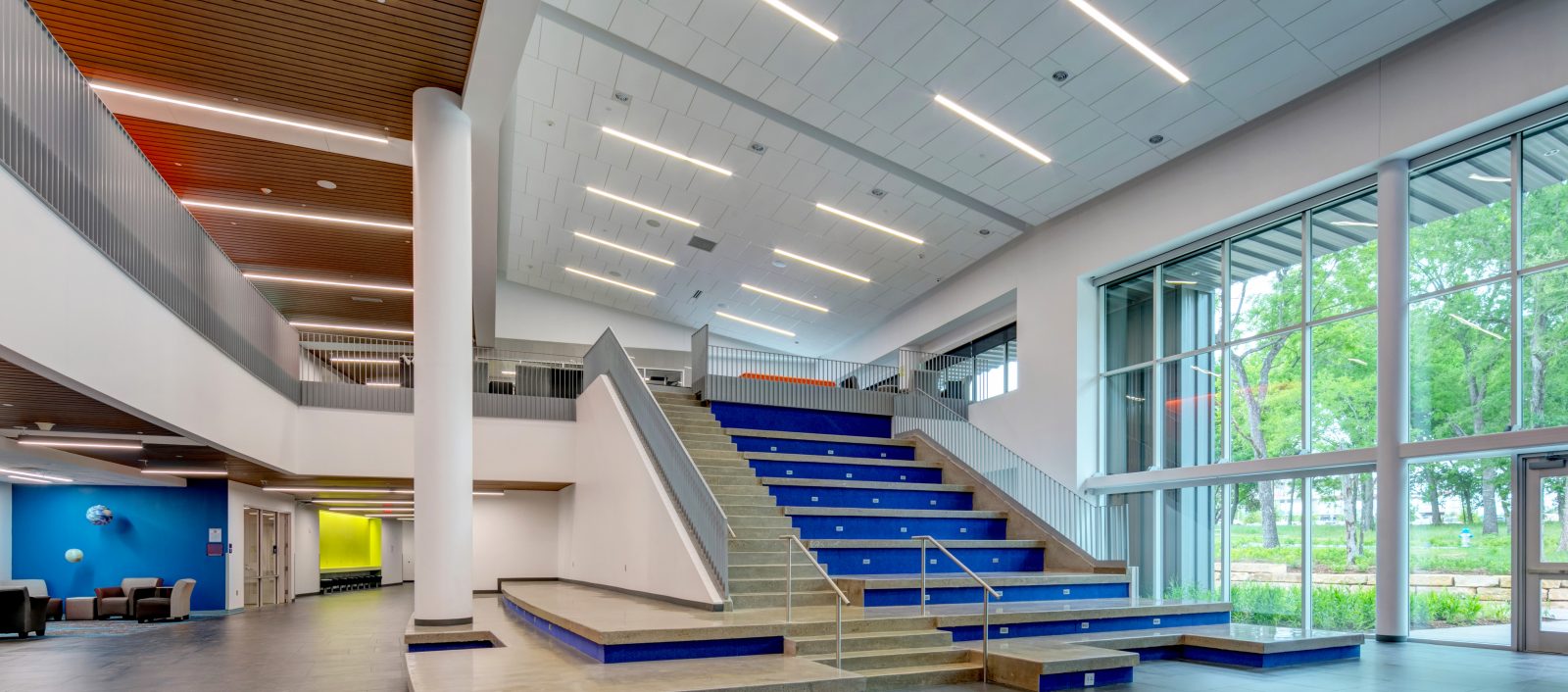 Interior view of the Allen ISD STEAM Center, featuring a modern open space with a central staircase, large windows, and contemporary lighting.