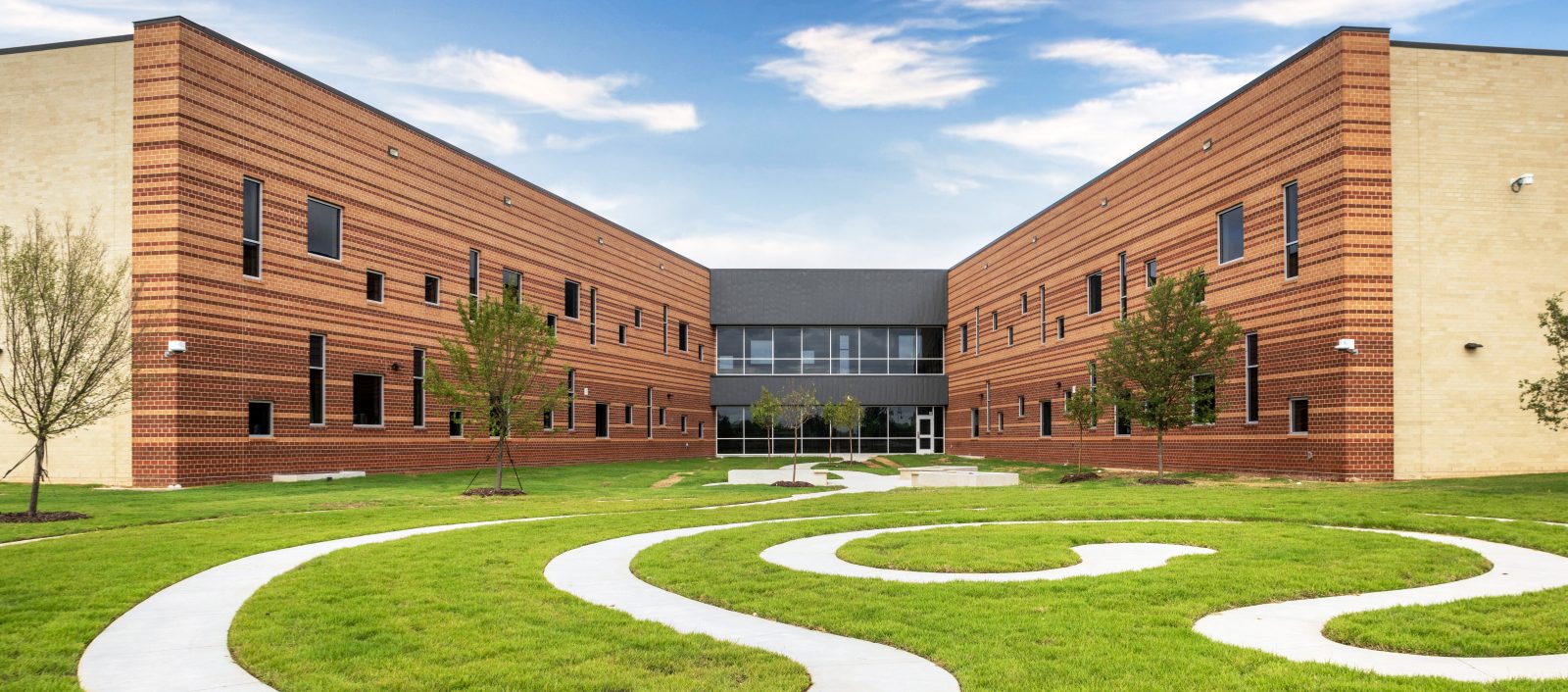 Courtyard at the Crowley Montessori Academy with a winding sidewalk surrounded by vibrant green grass and the building filling the background.