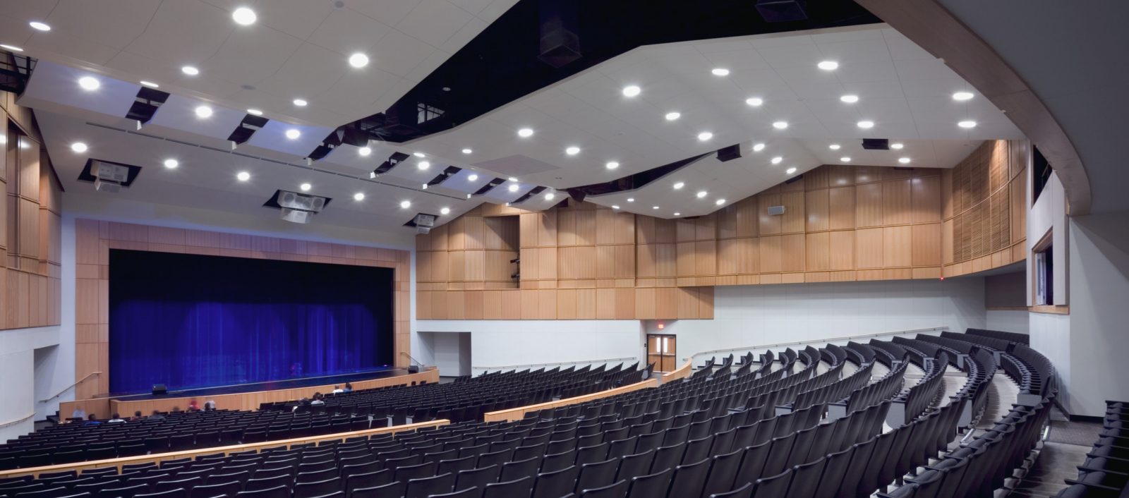 Lancaster ISD High School Auditorium with rows of seating, bright overhead lights, and a stage with blue curtains for performances.
